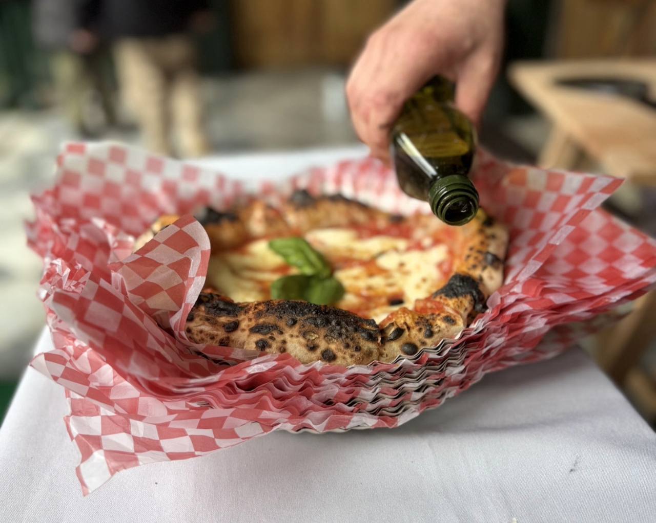 Pizza terminada en una canasta de servicio, recibiendo un toque de aceite de oliva.